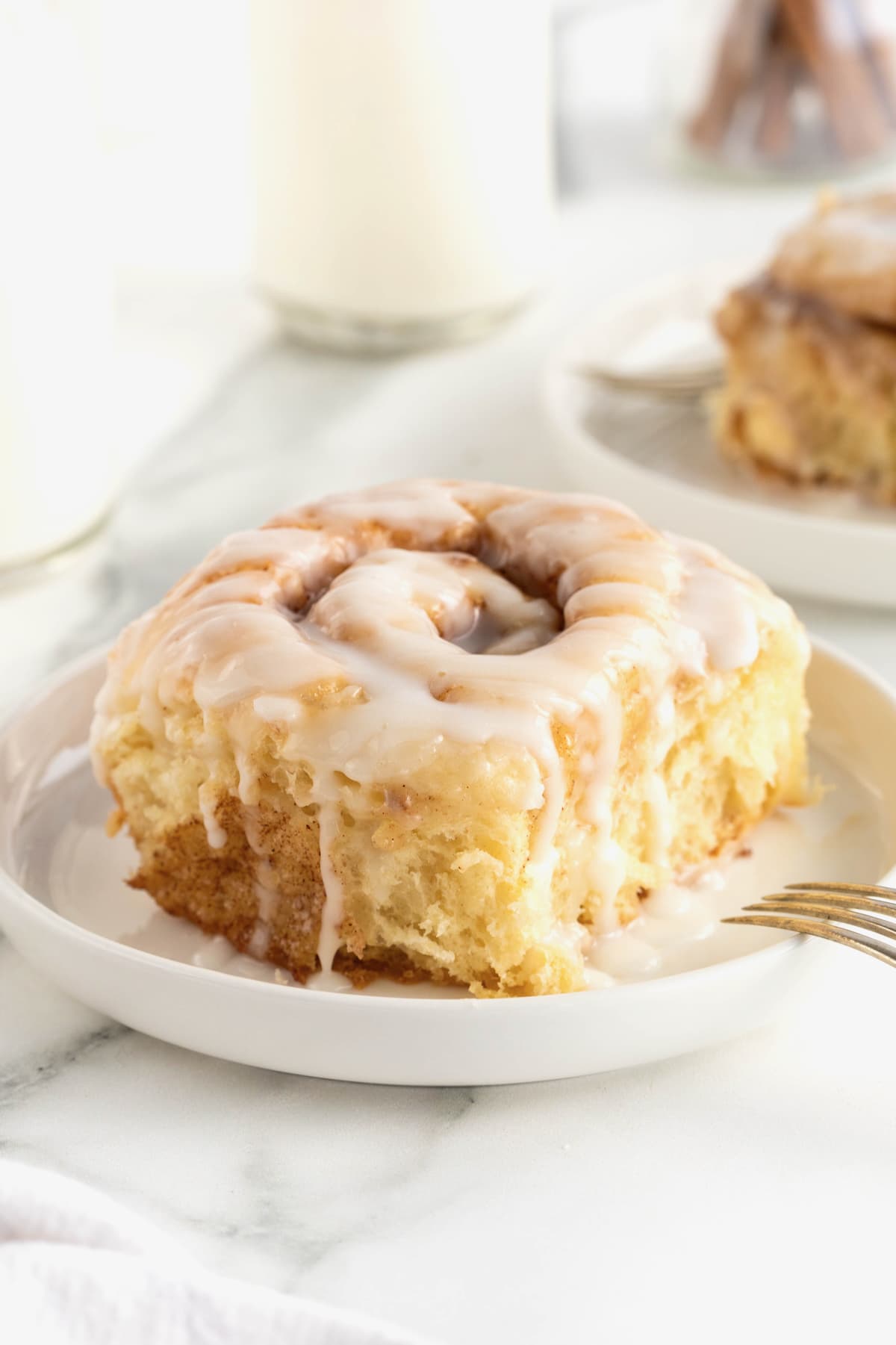 A homemade cinnamon roll on a small rimmed white plate.